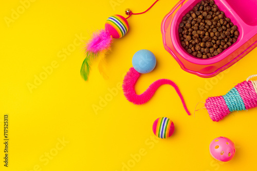 Cat bowl with dry food and toys on yellow background studio shot