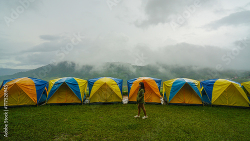 Women walk past camping Tent with flog and mountain view. Tent on campsite by the hill in rainy day. Raindrops on a tourist tent. Khao Kho, Phetchabun Province in Thailand. photo