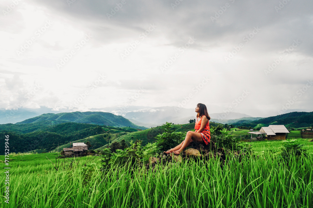 Beautiful Asian woman feel relaxing and enjoying in in the meadow. Green rice seedlings in a paddy field with beautiful sky and cloud.  Ban Pa Bong Piang, Chiangmai Province, Thailand.