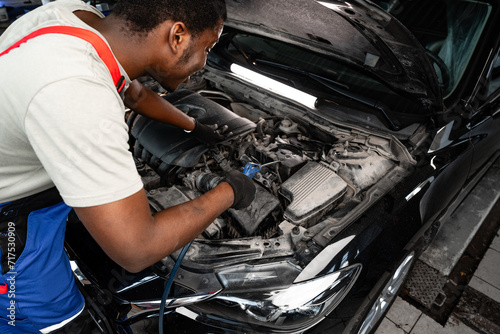 Young African auto mechanic checking car engine under the hood in auto service © fotofabrika