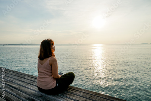Woman on wooden pier contemplating sunrise. Woman sitting on a jetty at an idyllic lake during sunrise.