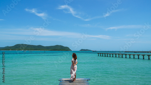 An evening shot of a tourist asian woman standing at the end of a pier looking in the water. young woman on wood bridge and sea beach at Sattahip, Thailand. Wood bridge beautiful. photo