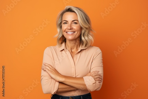 Portrait of happy mature woman with crossed arms over orange background.