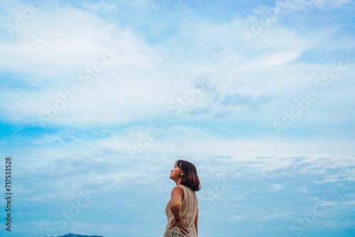 Portrait of woman looking up to the sky. Woman in summertime. Asian woman short hair and white sleeveless shirt looking up blue sky background on sunny day in summer.