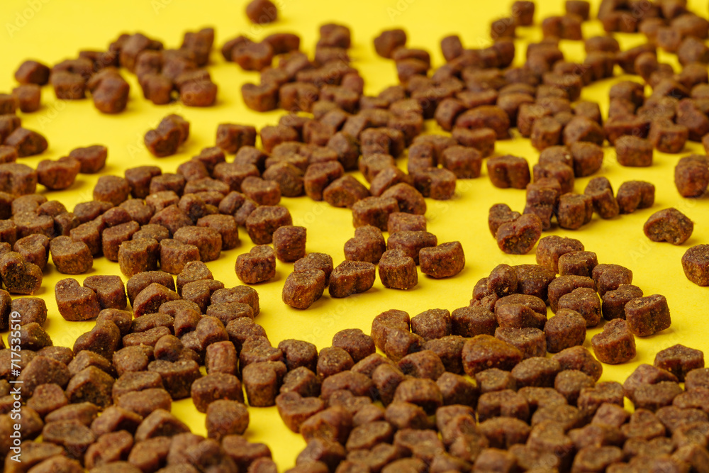 Obraz premium Dry cat food scattered on yellow background studio shot