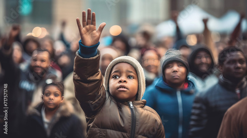 A black child with hands raised with a background of people demonstrating