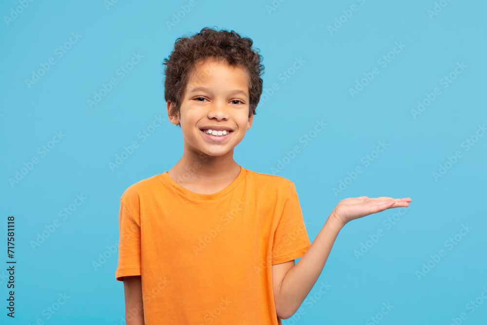 Happy boy presenting something with hand in orange shirt, blue background Happy boy presenting something with hand in orange shirt, blue background