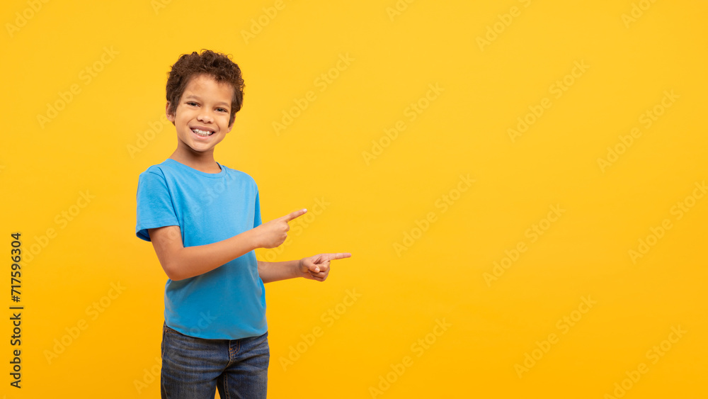 Happy boy smiling and pointing sideways at free space on yellow background Happy boy smiling and pointing sideways at free space on yellow background