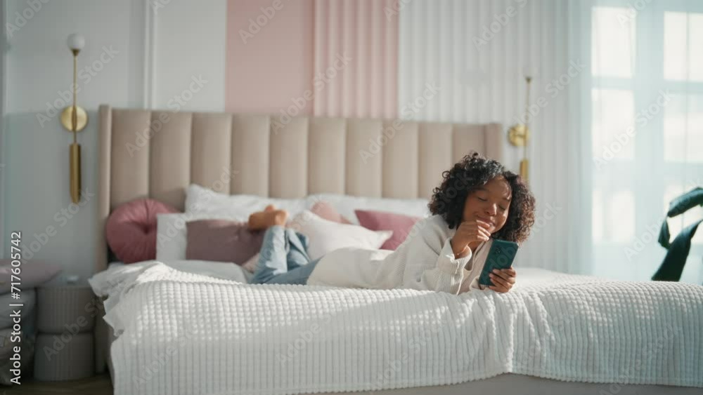 Contented african american teen girl reading typing messages in smartphone chatting with friends lying in bed. Smiling happiness curly relaxed teenager enjoying online communication in phone. Contented african american teen girl reading typing messages in smartphone chatting with friends lying in bed. Smiling happiness curly relaxed teenager enjoying online communication in phone.