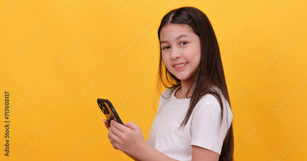 Cute little girl using smart phone on a yellow background.
