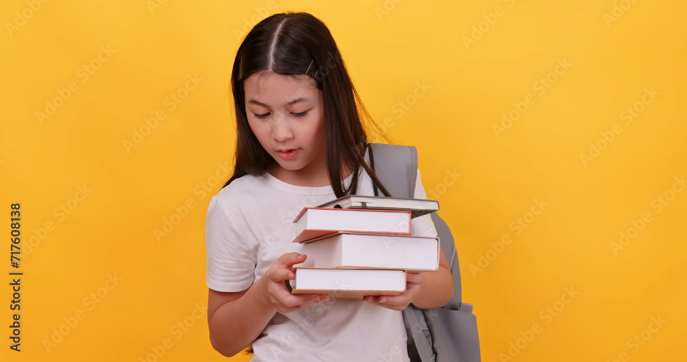 Fototapeta premium Cute school girl is carrying a school bag and holding a textbook on a yellow background.