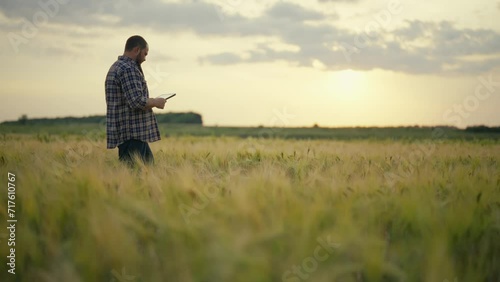Man botanist with tablet works in field. Farmer agronomist checks ripe wheat, growth, collects data. Scientist engineer conducts research of plant cultivation. Agribusiness, farm work concept.
