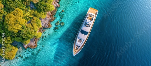 Panoramic top view photo of a yacht with a helicopter landing area in a tropical bay with turquoise open sea, captured by an aerial drone.