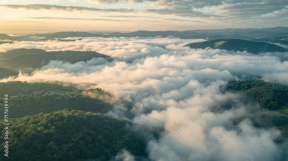 Aerial forest mountains landscape in the morning gold light with lots of low clouds into the valleys and a hazy sky