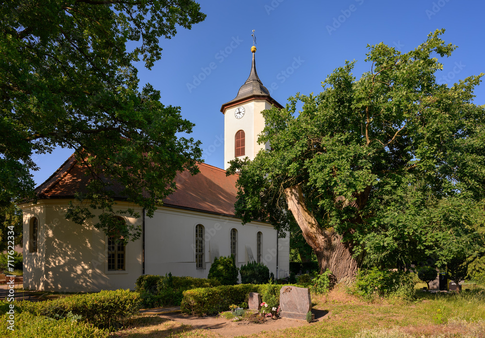 Im Schatten alter Bäume steht die denkmalgeschützte Dorfkirche Wustermark am 66-Seen-Wanderweg - Inschriften wurden retuschiert