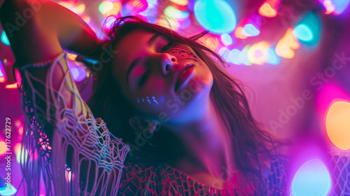 Beautiful uninhibited young woman wearing macrame clothes dancing in a nightclub with neon colors lights photo
