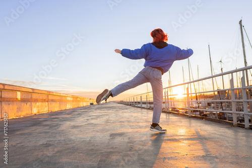 woman dancing in a port at sunset, red hair, smiling photo