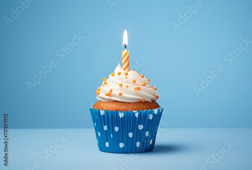 a white cupcake with blue polka dots with a blue candle on the background and a blue background