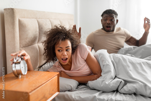 Shocked african spouses overslept looking at alarm clock in bedroom photo