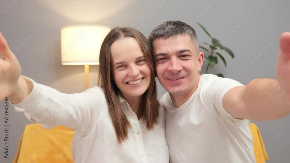 Love lives forever. Happy young adult spouses taking selfie enjoying spending time together while sitting on sofa and having fun smiling and laughing at camera pov Love lives forever. Happy young adult spouses taking selfie enjoying spending time together while sitting on sofa and having fun smiling and laughing at camera pov