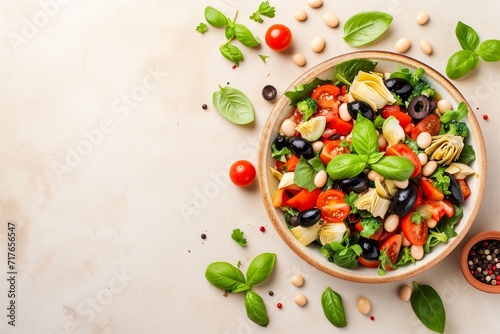 a top view on a bowl with colorful healthy salad with artichokes, tomatoes, lettuce, broccoli, olives and herbs on a beige colored concrete background, copy space for text