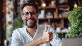 A satisfied businessman wearing glasses gives a thumbs up while using a laptop at the office