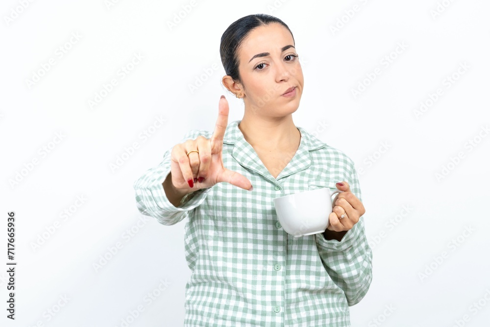 Beautiful young woman wearing green plaid pyjama making fun of people with fingers on forehead doing loser gesture mocking and insulting. Beautiful young woman wearing green plaid pyjama making fun of people with fingers on forehead doing loser gesture mocking and insulting.