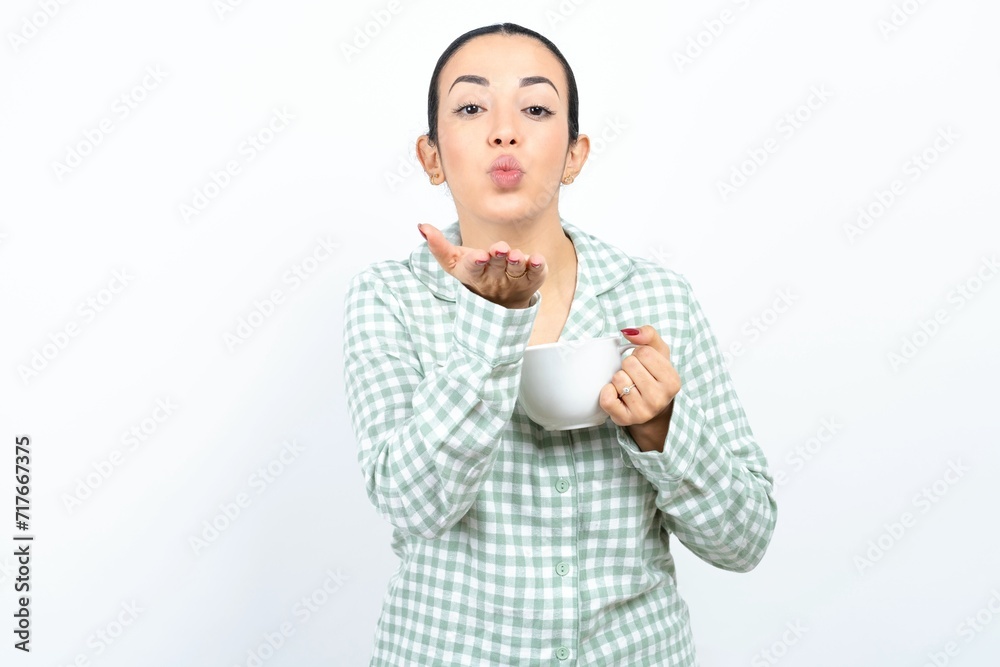 Beautiful young woman wearing green plaid pyjama looking at the camera blowing a kiss with hand on air being lovely and sexy. Love expression. Beautiful young woman wearing green plaid pyjama looking at the camera blowing a kiss with hand on air being lovely and sexy. Love expression.