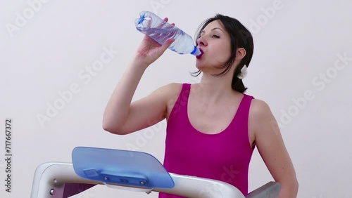 Young woman is exercising on a treadmill and drinking water to hydrate her body, Video Clip 4K