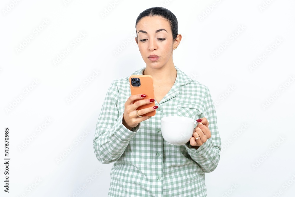 Focused Beautiful young woman wearing green plaid pyjama use smartphone reading social media news, or important e-mail Focused Beautiful young woman wearing green plaid pyjama use smartphone reading social media news, or important e-mail