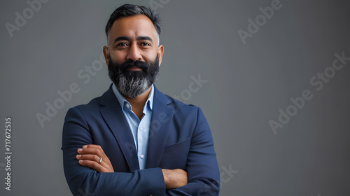 Standing alone on gray with his arms crossed is a proud, self-assured, bearded Indian businessman, investor, wealthy ethnic CEO, corporate executive, professional lawyer, and banker. picture photo
