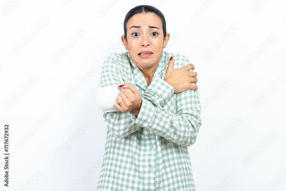 Desperate Beautiful young woman wearing green plaid pyjama trembles and feels cold, hugs oneself to warm up or feels scared notices something terrifying. Desperate Beautiful young woman wearing green plaid pyjama trembles and feels cold, hugs oneself to warm up or feels scared notices something terrifying.
