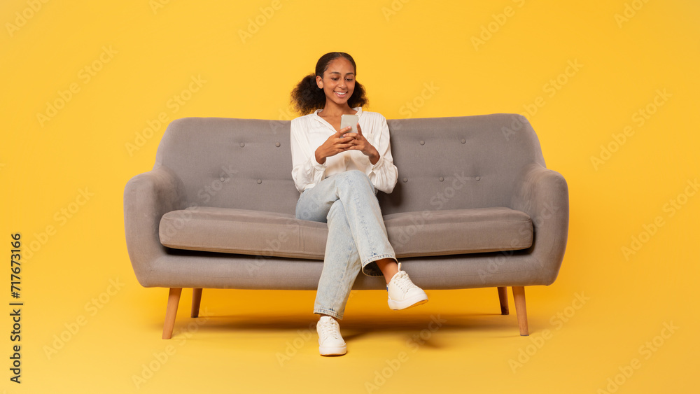 African american student teenager girl using smartphone on couch, studio African american student teenager girl using smartphone on couch, studio