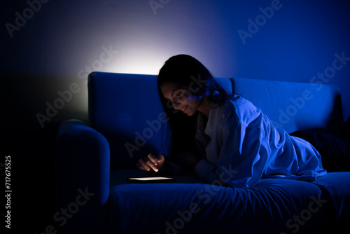 A person is lying on a couch, illuminated by the soft glow of a smartphone screen as they engage with social media in the tranquility of a nighttime setting.