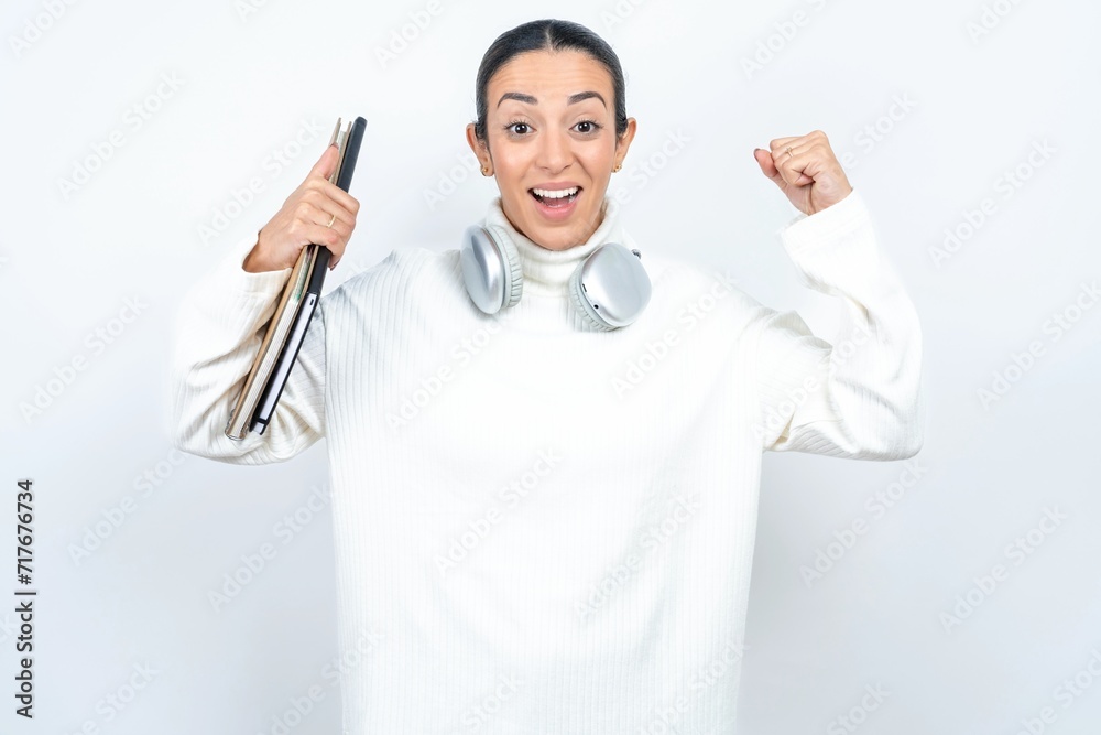 Shocked ecstatic Young beautiful woman wearing white turtleneck sweater win luck lottery raise hands up shout yea Shocked ecstatic Young beautiful woman wearing white turtleneck sweater win luck lottery raise hands up shout yea