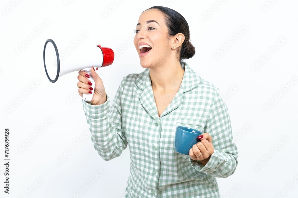 Funny Beautiful young woman wearing green plaid pyjama and holding a cup People sincere emotions lifestyle concept. Mock up copy space. Screaming in megaphone. Funny Beautiful young woman wearing green plaid pyjama and holding a cup People sincere emotions lifestyle concept. Mock up copy space. Screaming in megaphone.