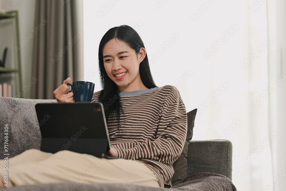 Carefree young Asian woman watching video on digital tablet. People, technology and lifestyle Carefree young Asian woman watching video on digital tablet. People, technology and lifestyle