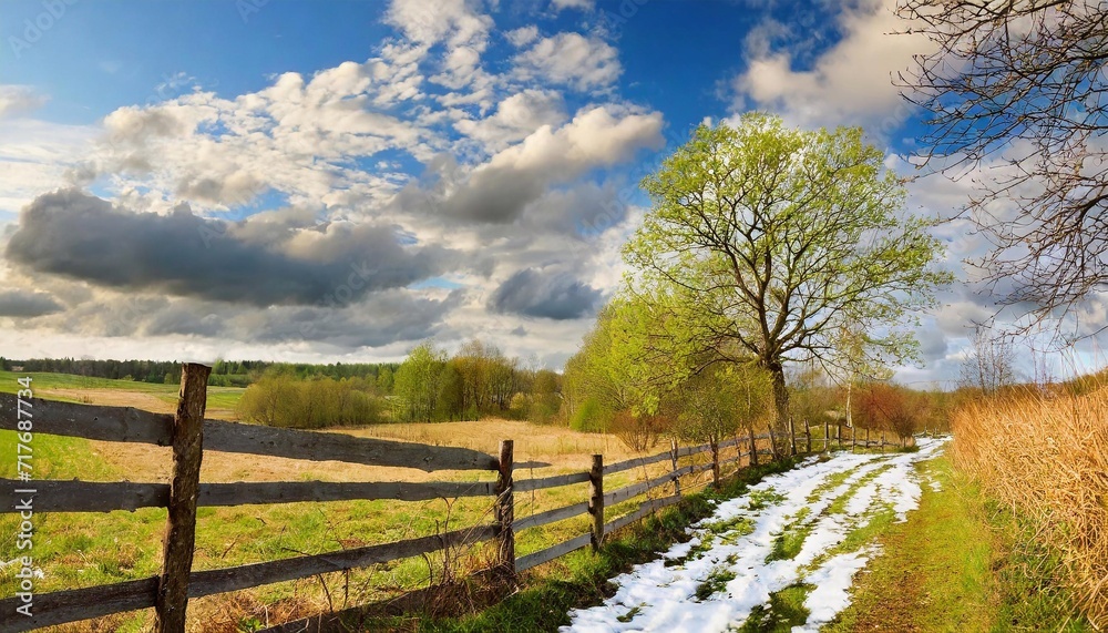 Early spring, old wooden fence along the road where the snow is parting. Rural landscape.