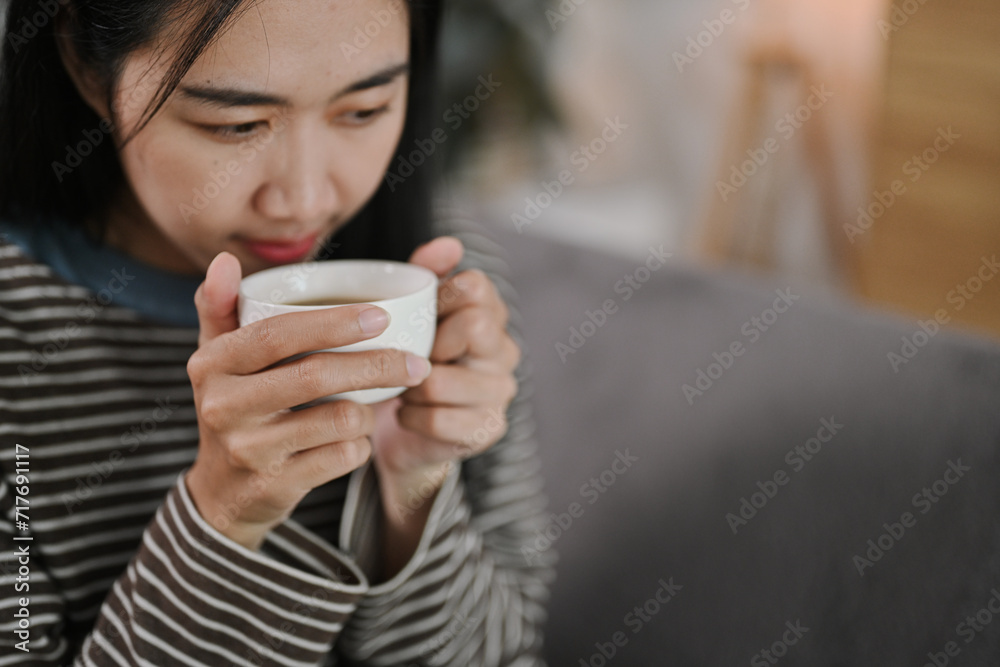 Happy young woman sitting on couch and enjoying her morning coffee in living room Happy young woman sitting on couch and enjoying her morning coffee in living room