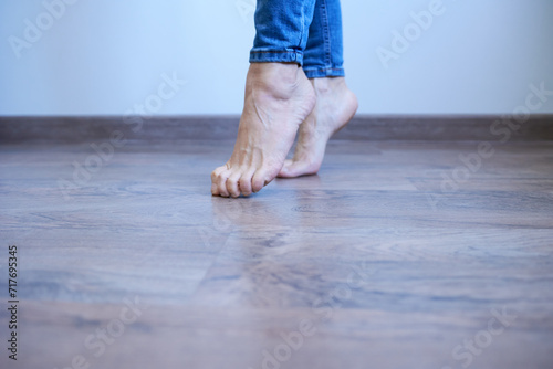 Barefoot girl in jeans standing on tiptoes indoors modern house. Women's legs close-up. Perfectly groomed feet. Enjoying the warm floor. photo
