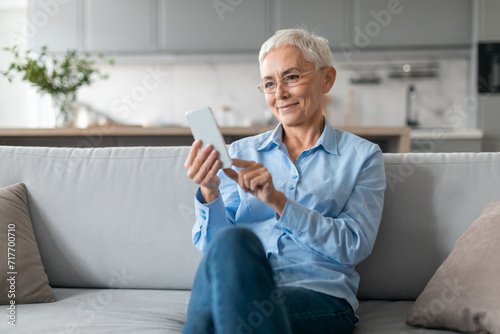 Senior Lady Wearing Eyeglasses Using Internet On Smartphone Texting Indoor