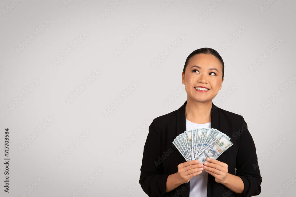 Optimistic Asian businesswoman holding and displaying a fan of US dollar bills Optimistic Asian businesswoman holding and displaying a fan of US dollar bills