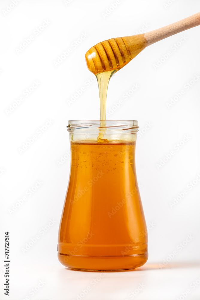 Honey drips from a spoon into a jar on white background Honey drips from a spoon into a jar on white background
