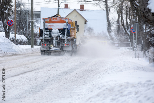 A snow-covered snowplow cleans the street after a snowfall, viw from back