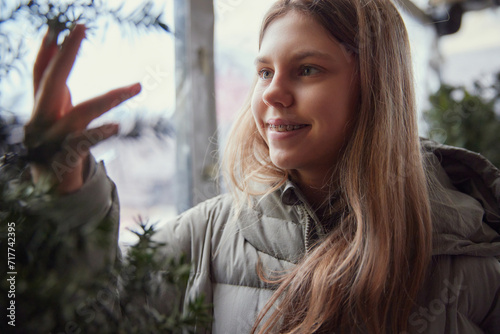 Portrait of smiling teenage girl with braces, touching touches fir branches. Blurred city background. Overcast. Selective focus. Concept of health care, medicine, lifestyle, dentist. Ad