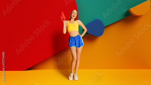 Health and wellness, promotion of sport drinks and comfortable sportswear. Energetic young woman in sportswear with water bottle on multicolored background. Sport, active and healthy lifestyle concept
