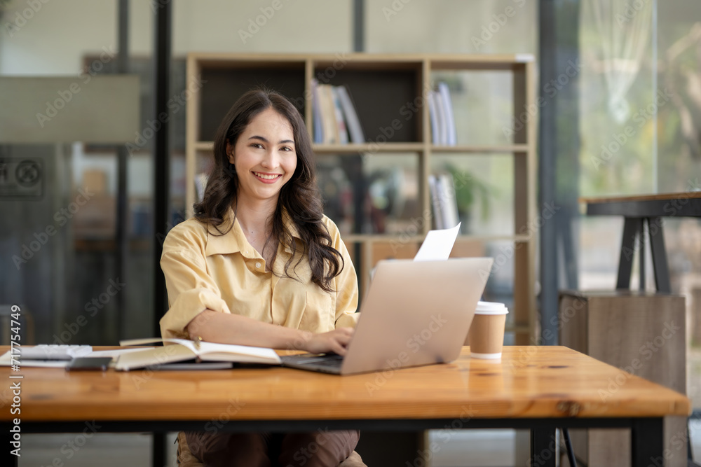 Attractive Asian businesswoman working with laptop and checking documents at table in office. Attractive Asian businesswoman working with laptop and checking documents at table in office.