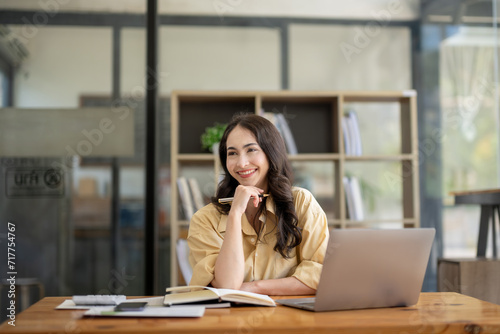 Attractive Asian businesswoman sitting with laptop and documents at table in office, thinking an ideas.