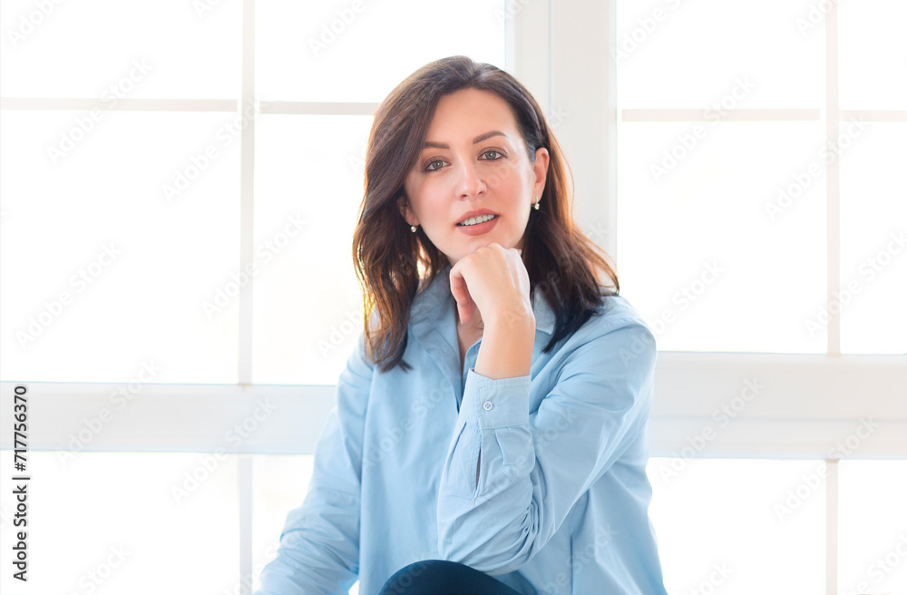 Brunette woman sitting by the window smiling at the camera Brunette woman sitting by the window smiling at the camera