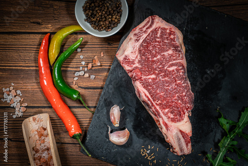 raw cowboy steak with seasonings on wooden background, prime rib eye on bone, top view